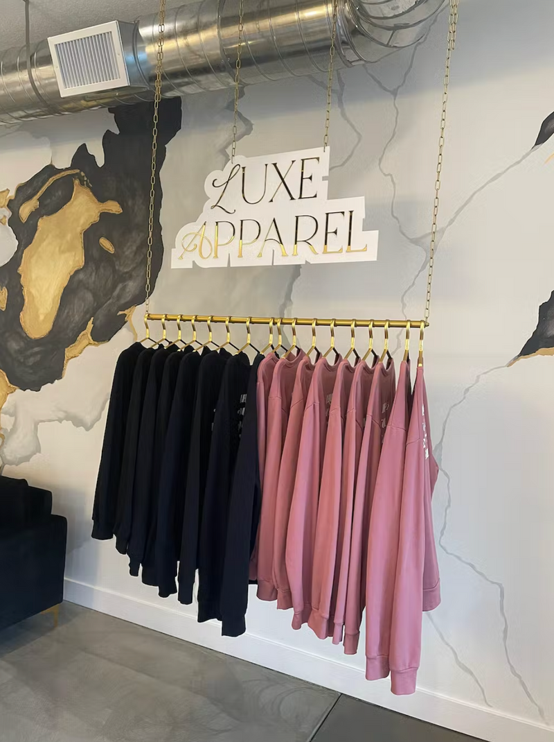 Clothing rack with black and pink shirts against a marble wall with 'Luxe Apparel' sign.