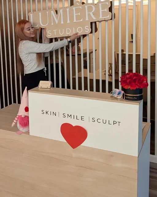 Person holding a sign above a reception desk with 'Lumiere Studios' branding.